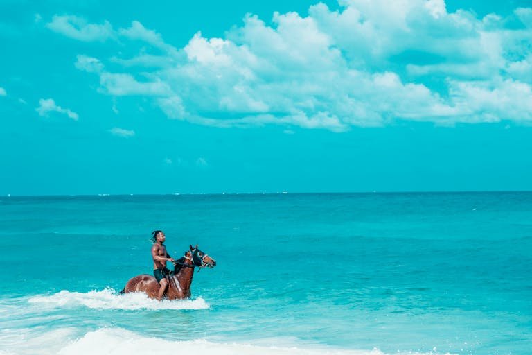 A man rides a horse through the vibrant turquoise waters of San Andrés beach, capturing a moment of serene adventure.