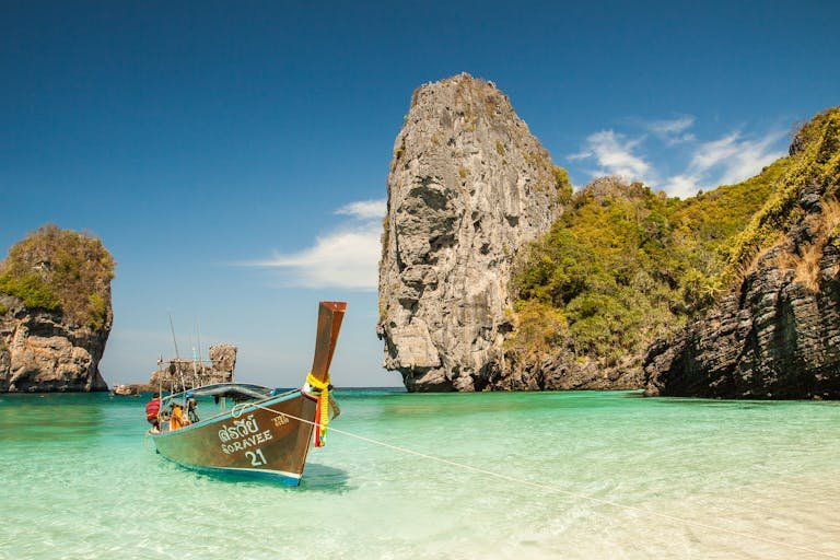 A picturesque tropical beach with a traditional boat and stunning limestone cliffs in clear turquoise waters.
