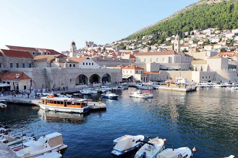 Explore the stunning Dubrovnik harbor with boats and historic architecture under a sunny sky.