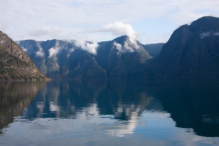 Peaceful lake reflecting mountain peaks, clouds, and blue sky, creating a tranquil nature scene.