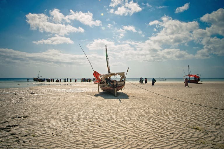 Traditional wooden boats anchored on a sandy tropical beach at low tide, under a bright blue sky.